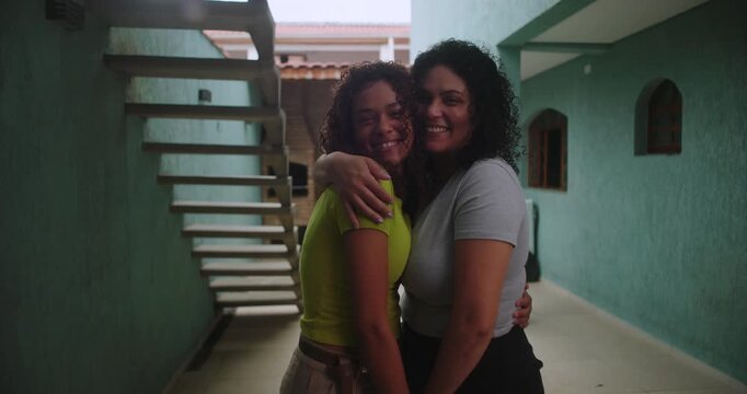 Mother and daughter of African descent standing together in a courtyard, smiling brightly and embracing, showcasing a close and joyful family relationship