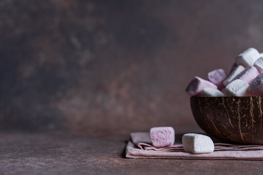 Close-up of a bowl of pink and white marshmallows on a napkin and concrete table