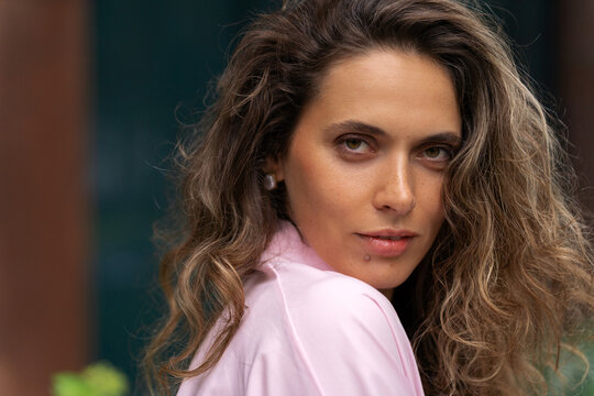Close-up side view profile of a confident young woman with long wavy curly brown hair looking over her shoulder