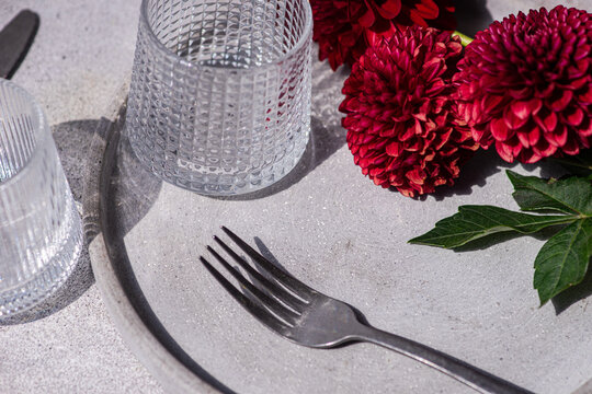 Close-up of a place setting with three dark red Pompon Dahlias on a grey concrete table