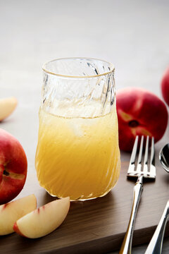 Close-up of a glass of Chilled Peach Juice with Fresh Peaches on a wooden chopping board