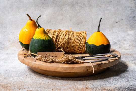 Close-up of three decorative mini pumpkins, a ball of string, scissors, burlap fabric and a gift tag with the word autumn on a Wooden board