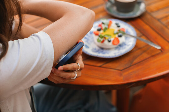 Close-up of a diabetic woman sitting at a table scanning a continuous glucose monitor sensor with her mobile phone before eating a meringue fruit dessert (pavlova)
