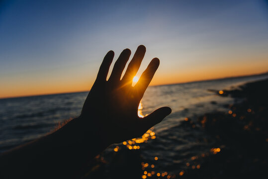 Silhouette of a man's hand reaching for the sun on a beach at sunset, Russia