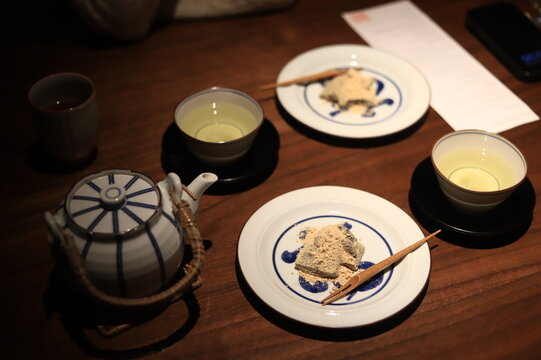 Overhead view of brown sugar flavoured bracken starch dumplings (warabi mochi) with cups of green tea on a table