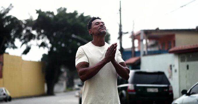 Man smiling with clasped hands, looking upward in faith and gratitude, expressing hope and devotion in a serene outdoor moment, deeply connected to spirituality