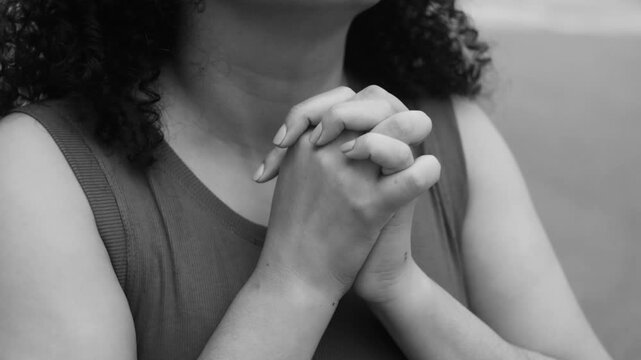 Close-up of woman in monochromatic scene with hands clasped in deep prayer, expressing faith, spirituality, devotion, and emotional reflection