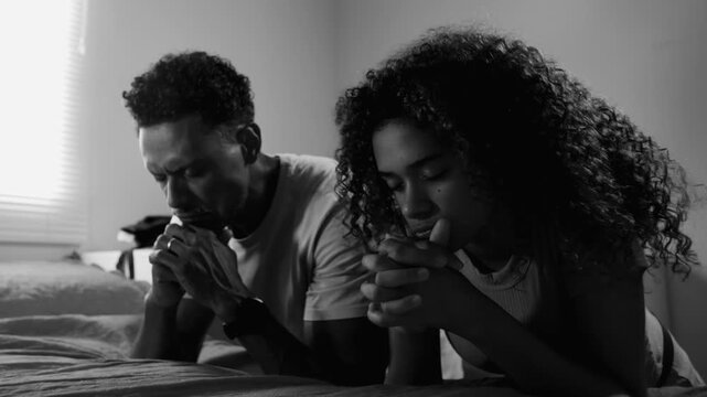 Father and teenage daughter kneeling in monochromatic scene, hands clasped, eyes closed, deep in prayer, expressing faith, spirituality, connection, hope, and devotion