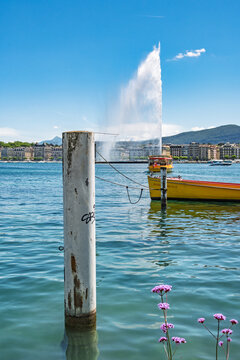 Le Jet d'eau de Gen&egrave;ve jaillissant dans la rade avec une barque jaune et un poteau en bois au premier plan