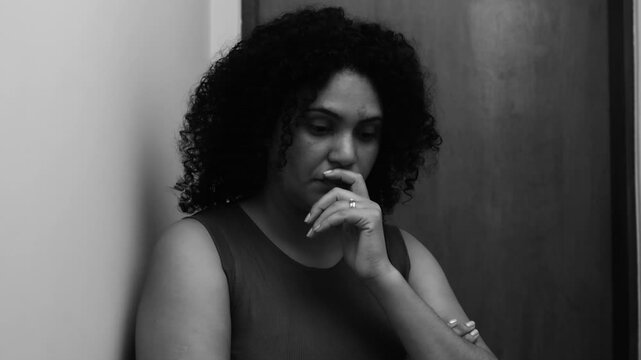 Woman standing in monochromatic scene, hand near mouth in deep contemplation, introspective expression, reflecting on emotions, concerns, and personal struggles