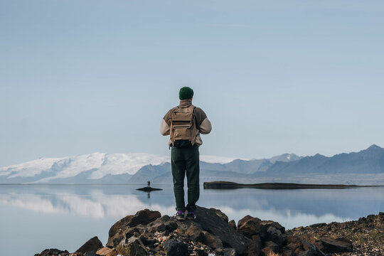 Man with backpack looking at glacier across mountain lake