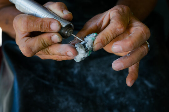 Artisan hands carving gemstone with rotary tool in workshop