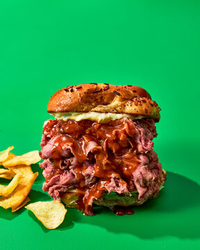 Roast beef sandwich with slaw, BBQ sauce and beer on green background.
