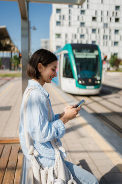 Woman use a phone and waiting for the tram at the station