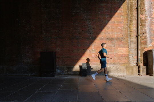 Young man running urban street sunlight shadow