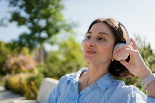 A pensive woman listens to music with headphones in a park