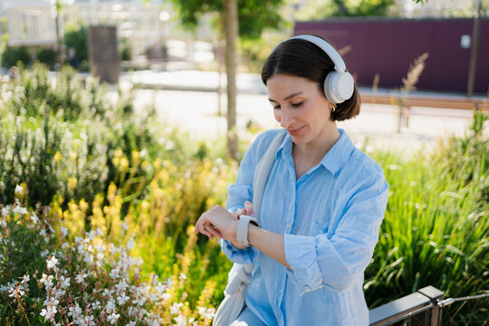 A woman using a smartwatch and  headphones at the city park