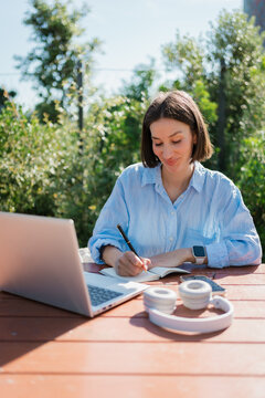 Freelancer Writing Ideas in Journal While Working on Laptop
