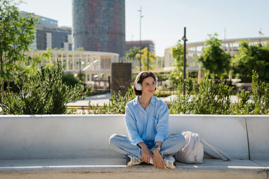 A woman listens to music with headphones in a city garden