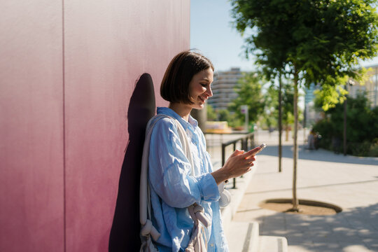 A woman uses a smartphone near a violet wall