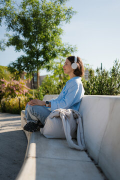 Pensive Woman Listening to Relaxing Music on Park Bench in Spring