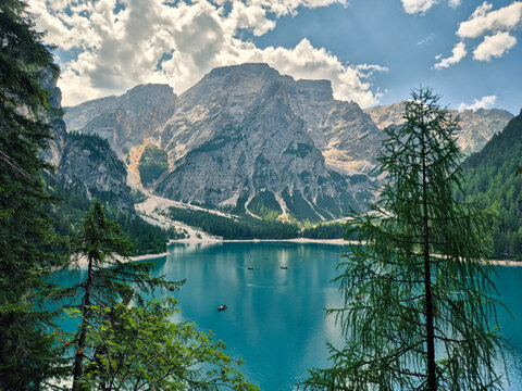 A breathtaking view of Lago di Braies in Dolomites, reflecting the dramatic, rugged mountain peaks under a cloudy but bright sky. 