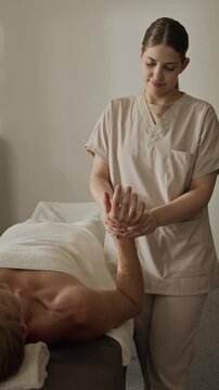 Vertical video of Caucasian young adult female therapist massaging wrist of Caucasian young adult male. Ideal for physical therapy advertising, rehabilitation clinic promo, and wellness branding