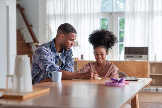 A father helps his daughter with schoolwork at home