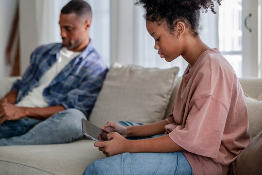 Father and daughter using personal devices on the sofa