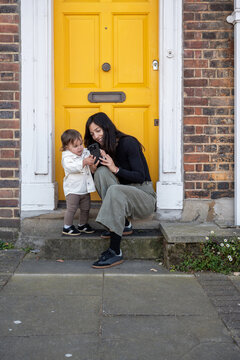 Mother Showing Smartphone To Baby Outside London Home