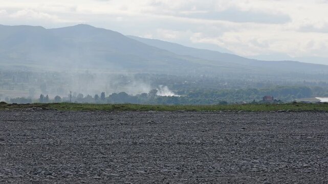 Rural landscape with smoke rising from a fire in a distant valley, misty mountains in the background