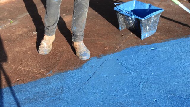 Pessoa pintando piso de azul com rolo de pintura durante reforma de casa simples no interior do Brasil