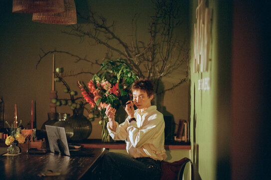 Woman adjusts makeup at laptop iin flower shop before work shift