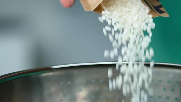 Hand pouring uncooked white rice from a paper bag into a stainless steel colander