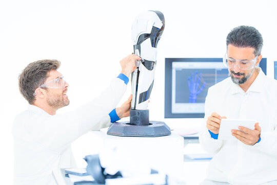 Sensor driven robotics research: a scientist points out a joint encoder on the base of a laboratory robot arm while his colleague keeps a hand on the upper segment