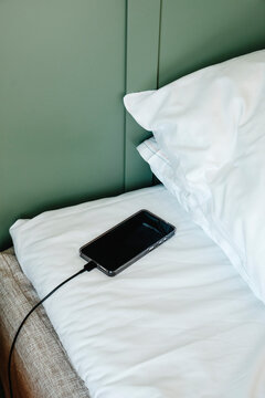 a smartphone connected to a charging cable rests on a bed