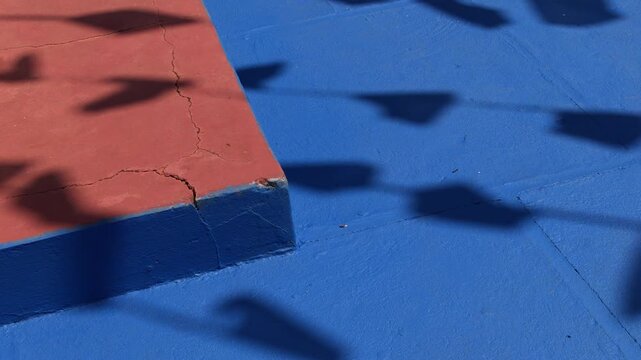 Sombras de bandeirinhas de festa junina projetadas sobre piso azul, textura abstrata da cultura popular do interior do Brasil