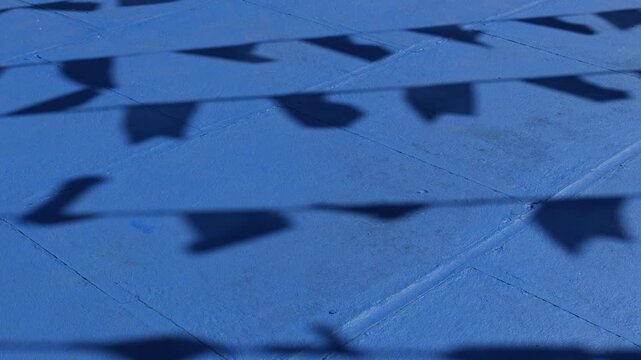 Sombras de bandeirinhas de festa junina projetadas sobre piso azul, textura abstrata da cultura popular do interior do Brasil