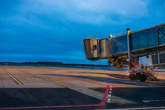 Airport jet bridge waiting on the runway apron under twilight blue sky