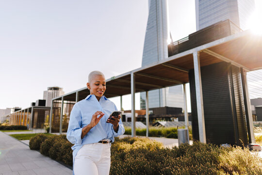 Smiling woman using smartphone in modern city park