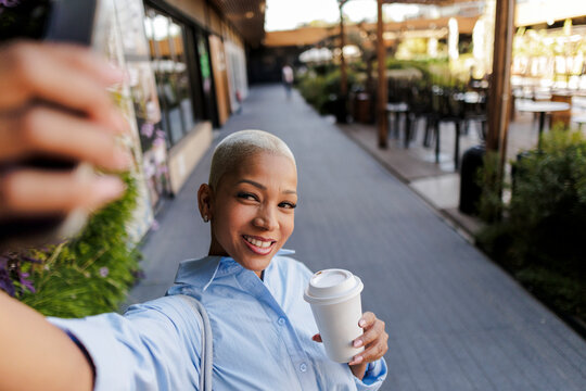 Smiling woman taking selfie holding coffee cup on urban street