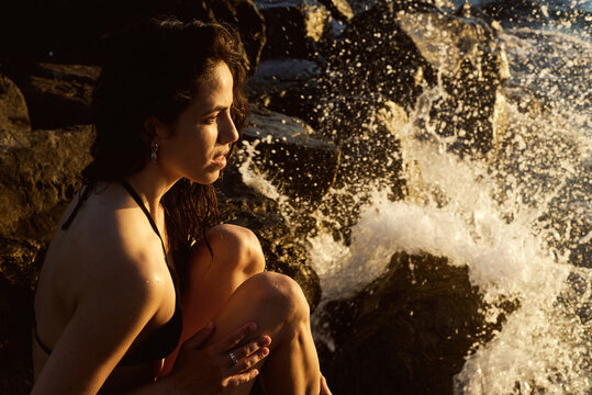 Woman sits on rocks by the sea while waves crash around