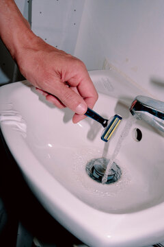 after shaving, a man brings his razor under a running bathroom faucet