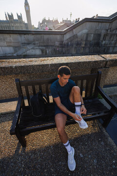 Young man tying shoelace on bench near Big Ben