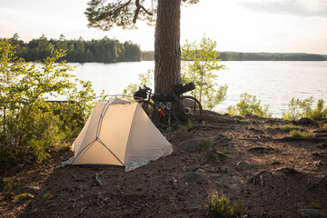 Camping tent and bicycle by tree next to lake © FOLIO