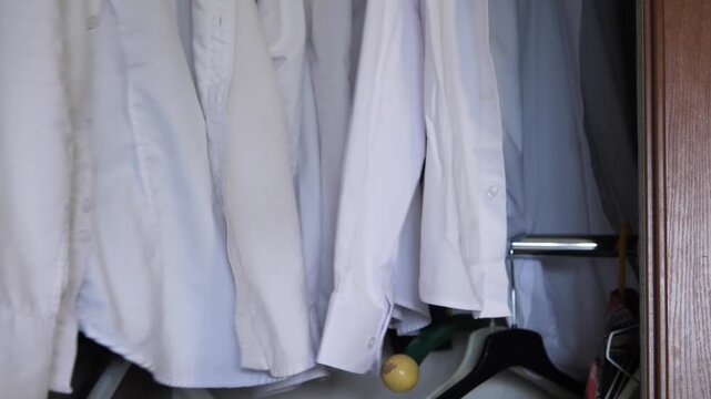 Close-up of a hand putting a shirt in a closet and closing the closet where white shirts and a blue jacket are hanging