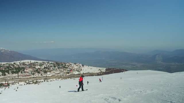 A snowboarder descends a snow-covered mountain, enjoying the winter sports activity. The scene captures the beauty of a clear day at a ski resort with a village in the background.