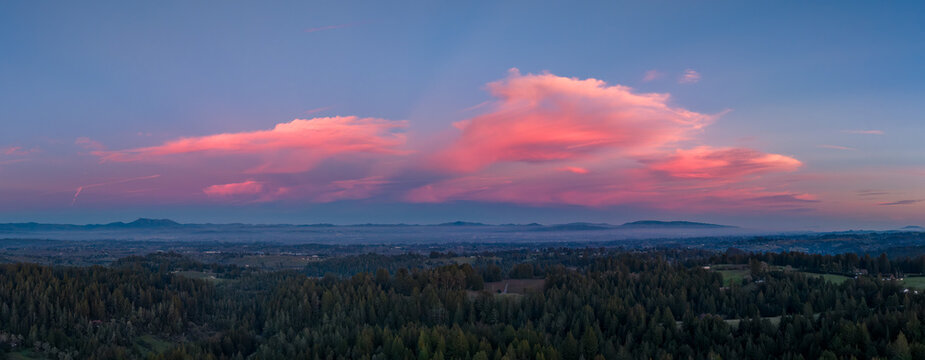 Panoramic view of Sonoma County, California landscape featuring lush green forests, rolling hills, and vibrant pink clouds at sunset over the distant mountains