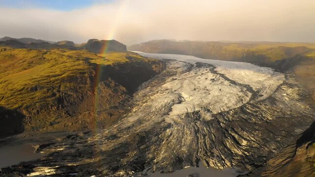 Aerial view of a glacier with a rainbow over mossy mountains, Iceland.
