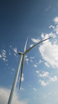 Wind turbine blades rotating against a blue sky with clouds, generating renewable and sustainable green energy for the future